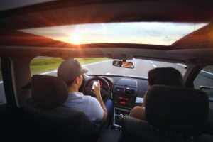 man driving looking at phone with woman